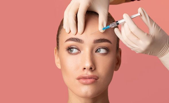 A woman is getting a botox injection in her forehead.