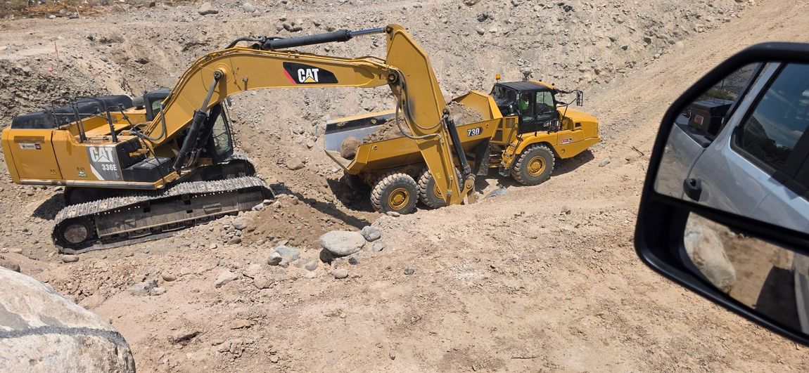 Yellow excavators digging in a rocky construction site, viewed from a vehicle window