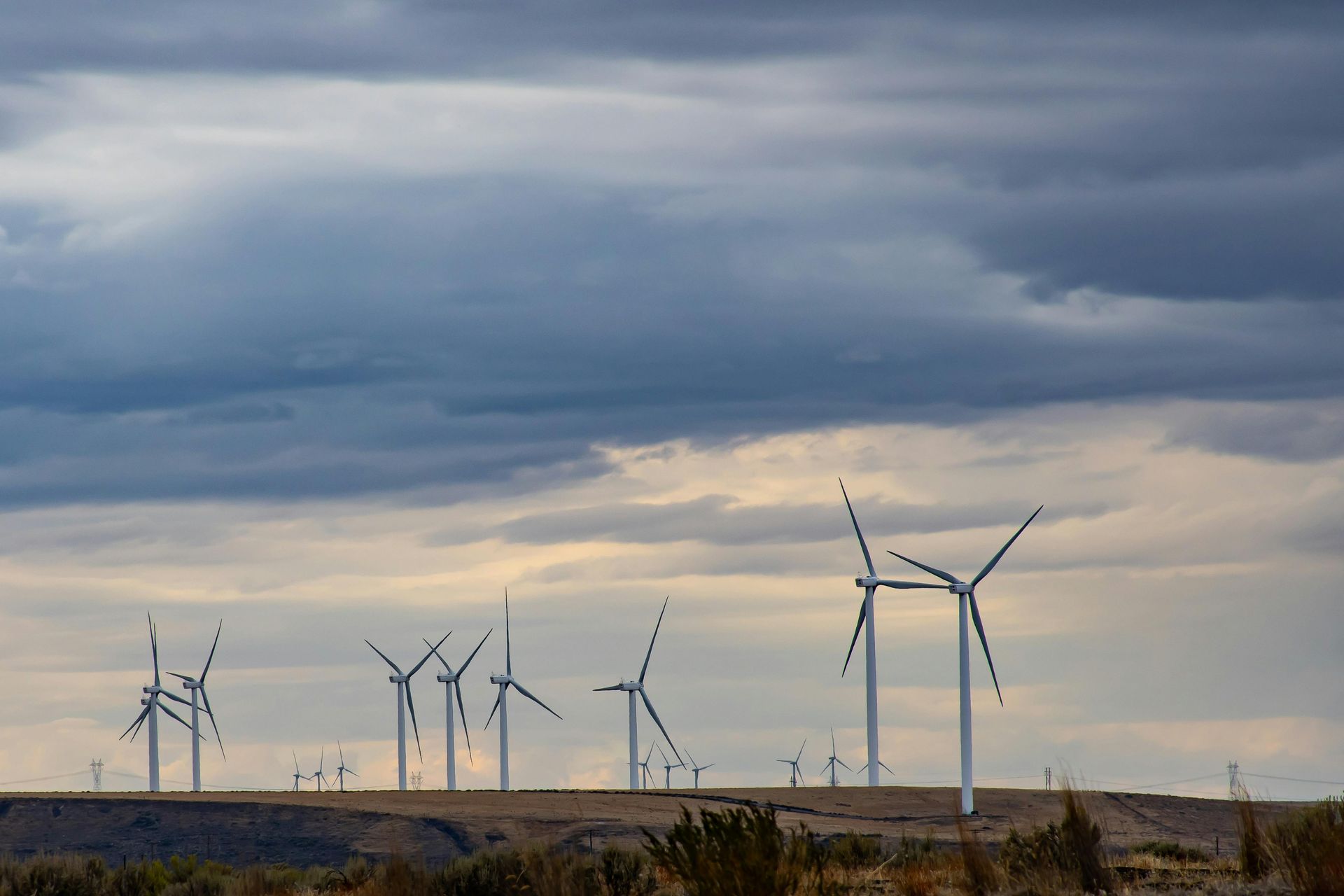 A row of wind turbines on top of a hill under a cloudy sky.