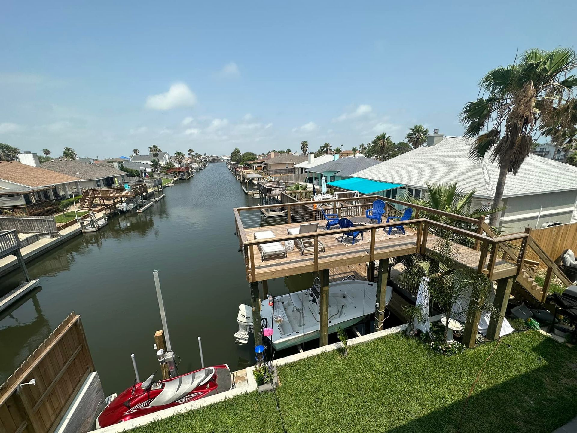Canal with houses, docks, boats, and a deck with blue chairs on a sunny day.