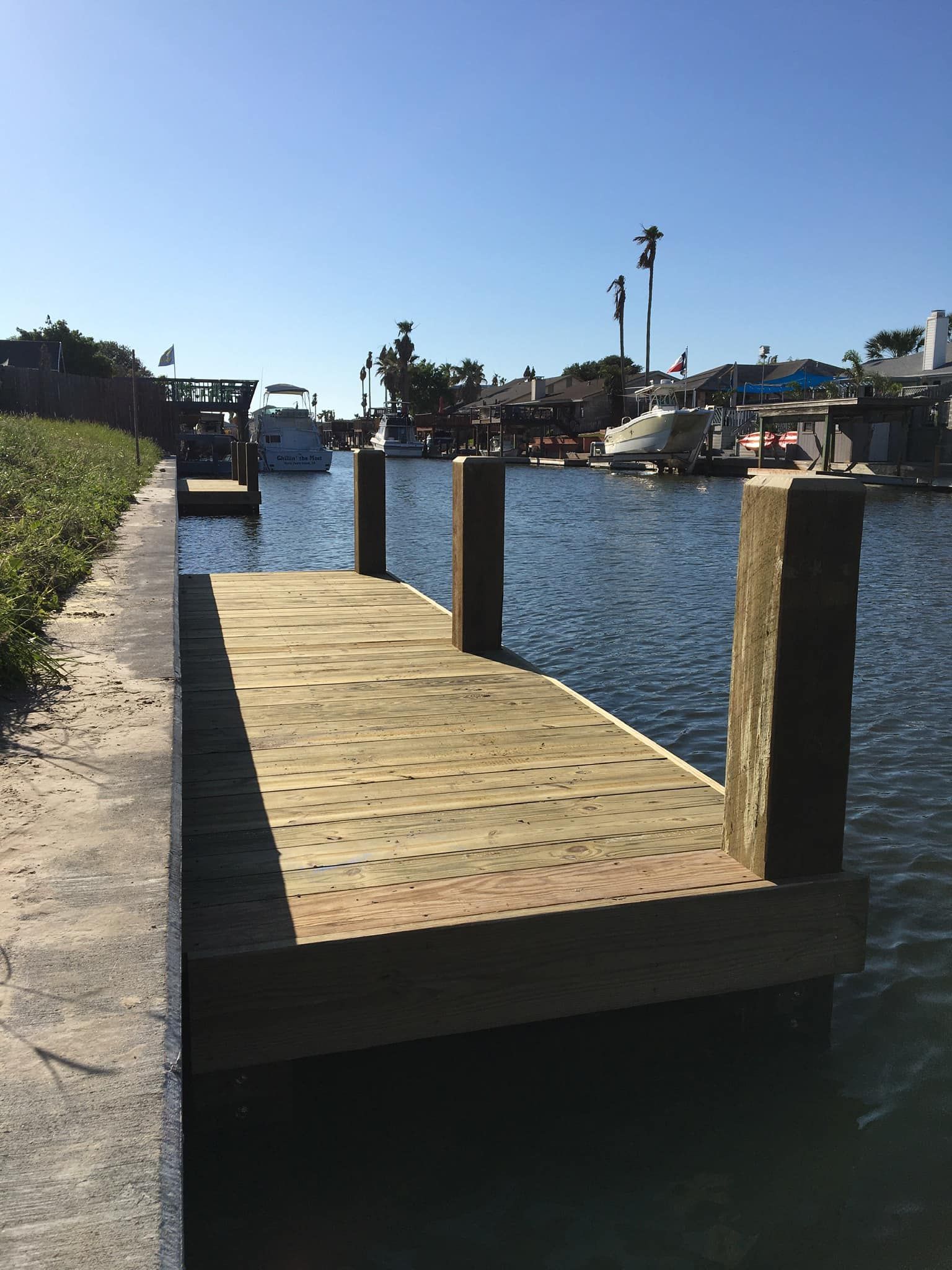 Wooden dock extending into water, boats visible, clear sky.