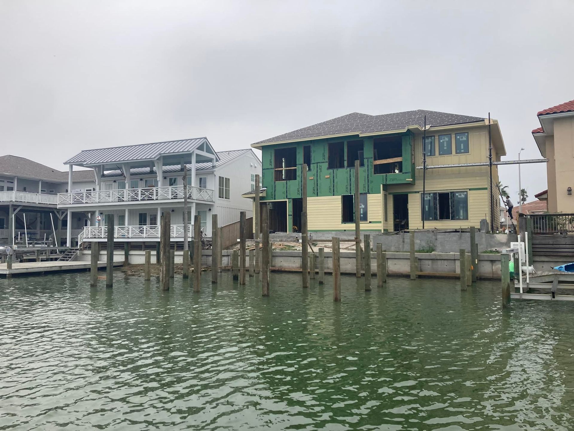 Houses on stilts along a waterway; one in construction. Cloudy, greenish water.