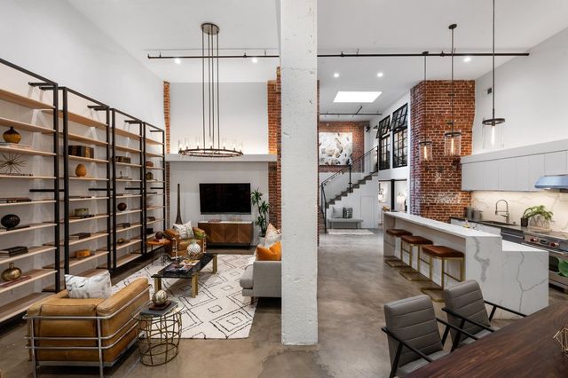 Modern open-plan loft with brick walls, shelving, white kitchen, and lounge seating