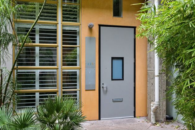 Gray door with small window beside large barred window in an orange exterior wall, framed by green bamboo.