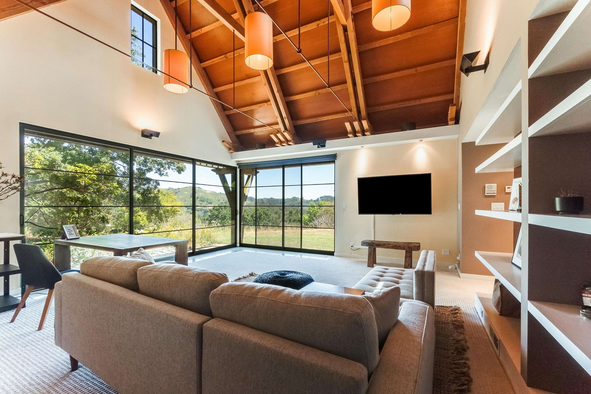 Modern living room with high wood ceiling, large windows, gray sofa, and wall-mounted TV