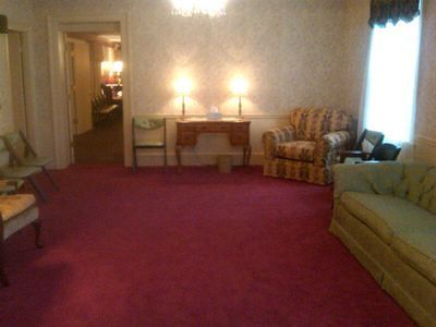 Living room with red carpet, sofas, armchairs, and two lamps by a window