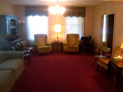 Cozy living room with red carpet, two armchairs, sofa, lamp, and wall mirror.