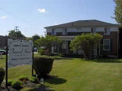Brick house with manicured lawn and a white sign reading “Grosvenor Hall” under a clear blue sky