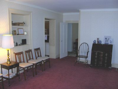Empty room with red carpet, white walls, chairs along the left wall, and a black dresser on the right.