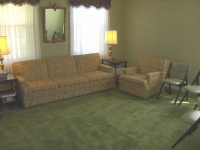 Living room with tan sofa, armchair, lamps, mirror, and green carpet.
