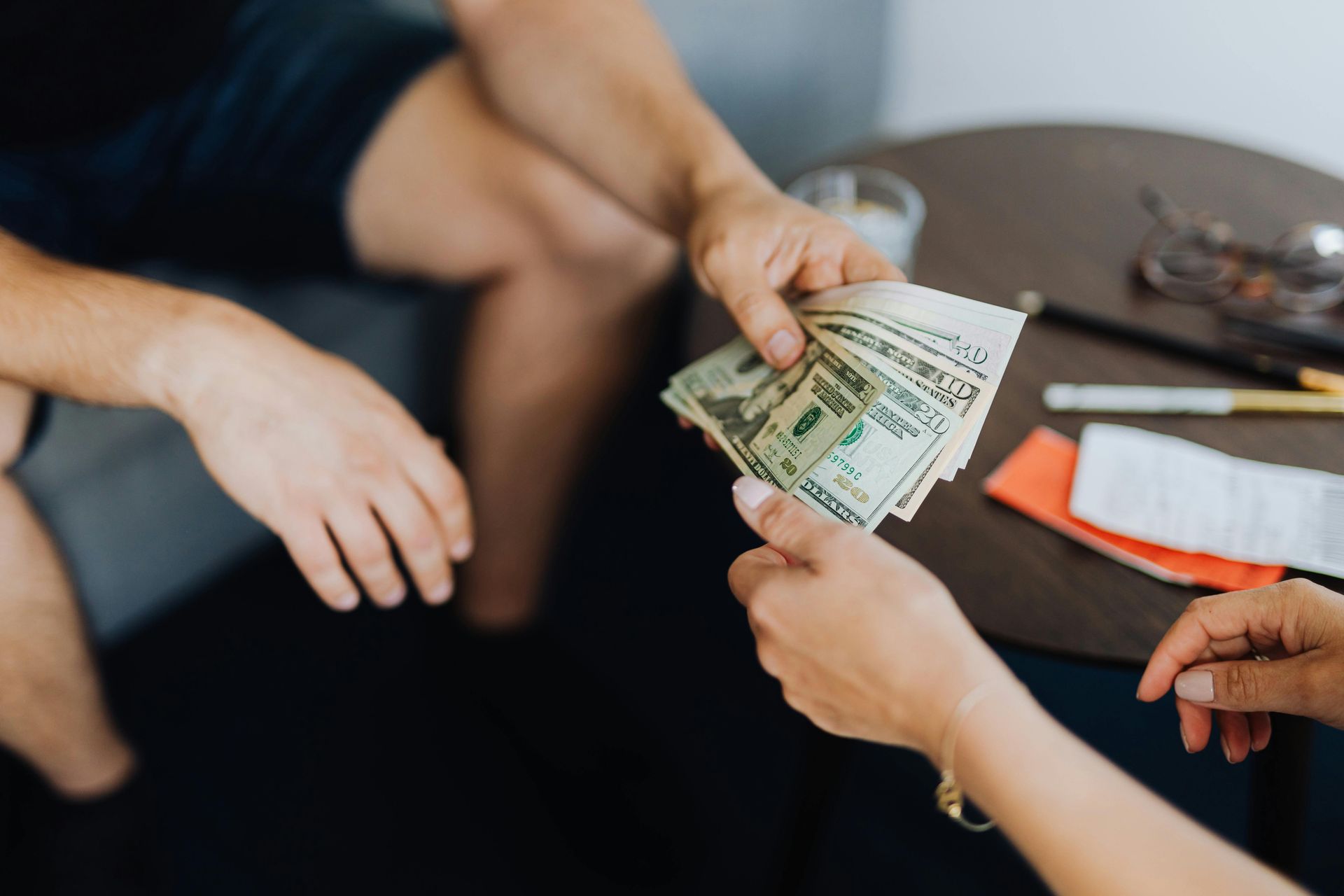 Person handing a stack of US dollar bills to another person.