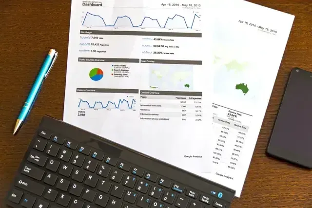 A desk with printed reports, keyboard, pen, and a smartphone, likely displaying data analysis charts.
