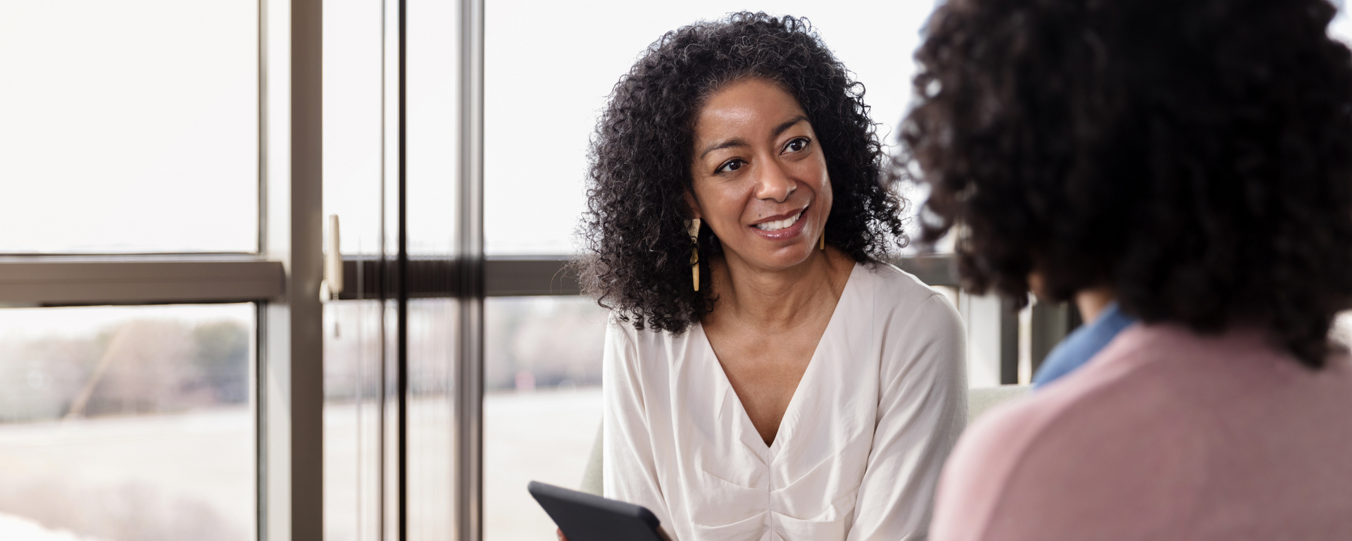 Two people talking in a bright room, one smiling while holding a tablet.