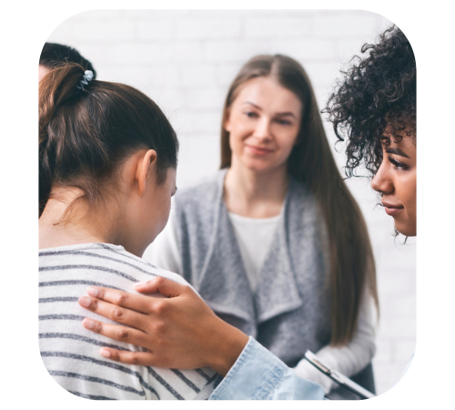 Person comforting another in a group therapy session with a counselor in the background