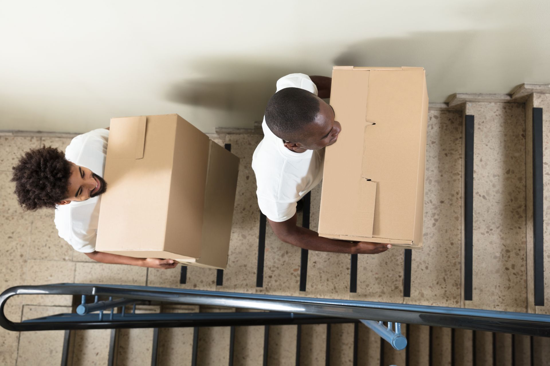 Two people carry boxes up a staircase; overhead view.