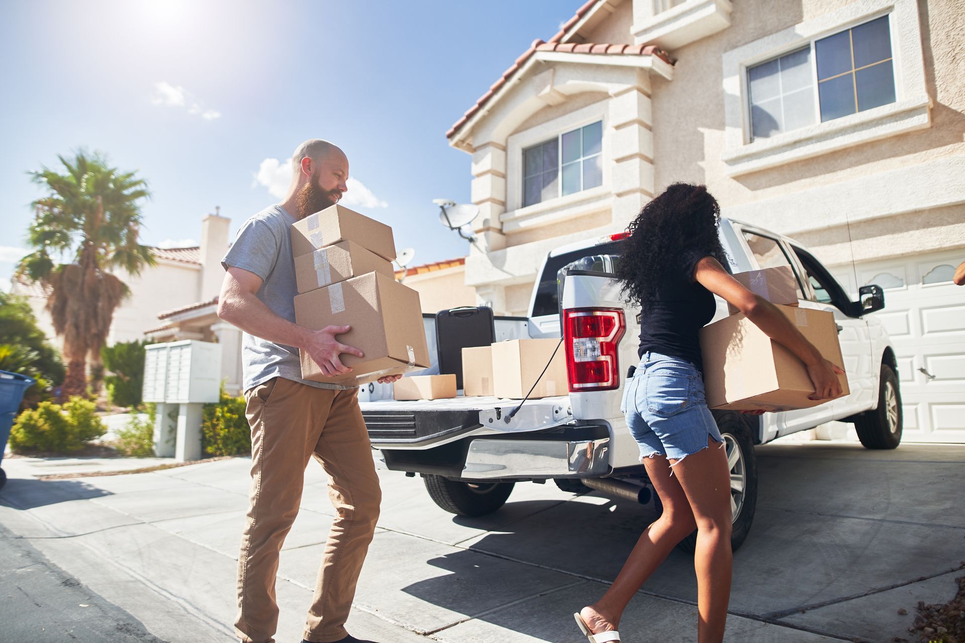 Couple loading boxes into a pickup truck in front of a house on a sunny day.