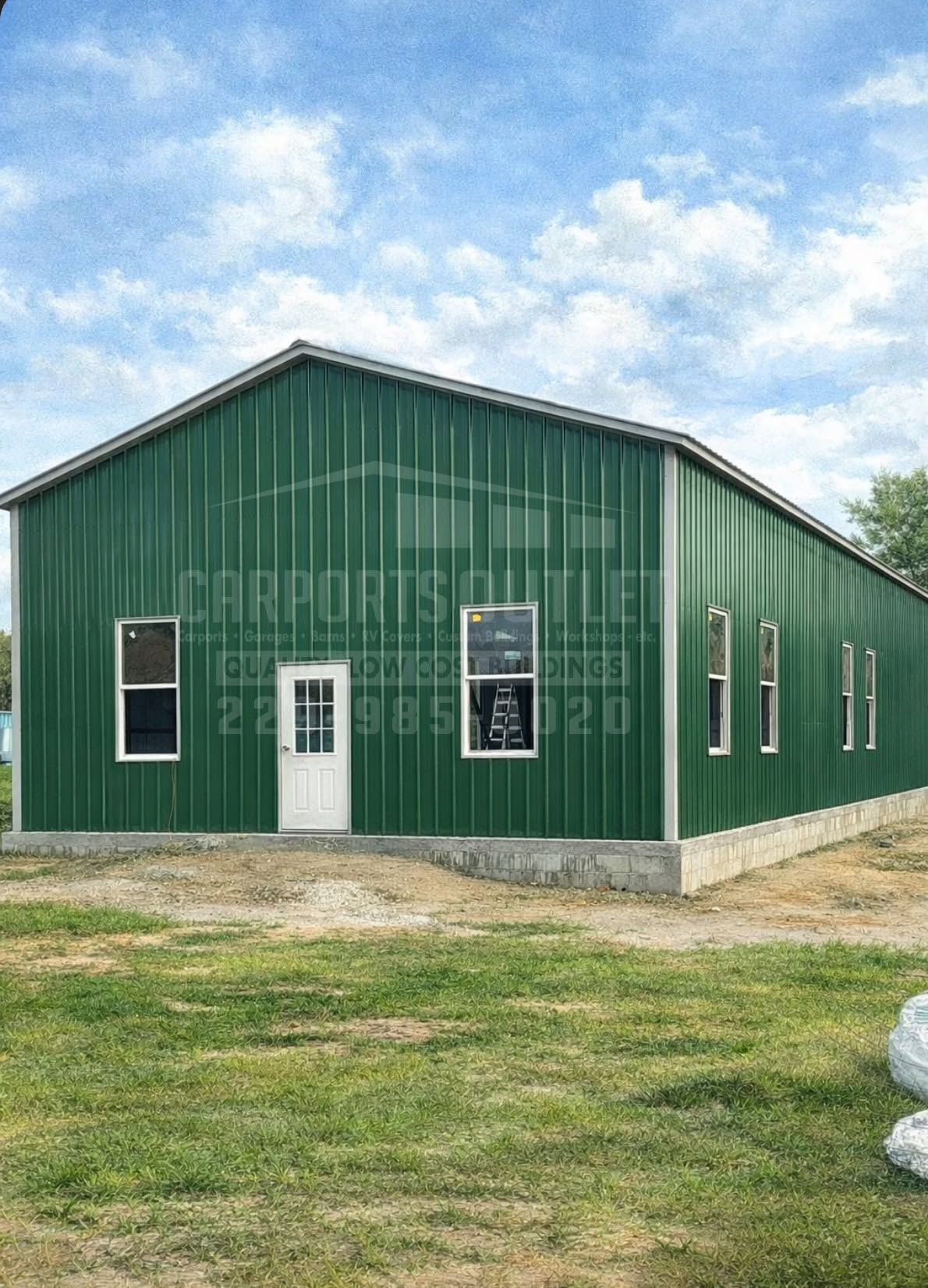 Green metal building with white doors and windows on a concrete foundation under a cloudy sky