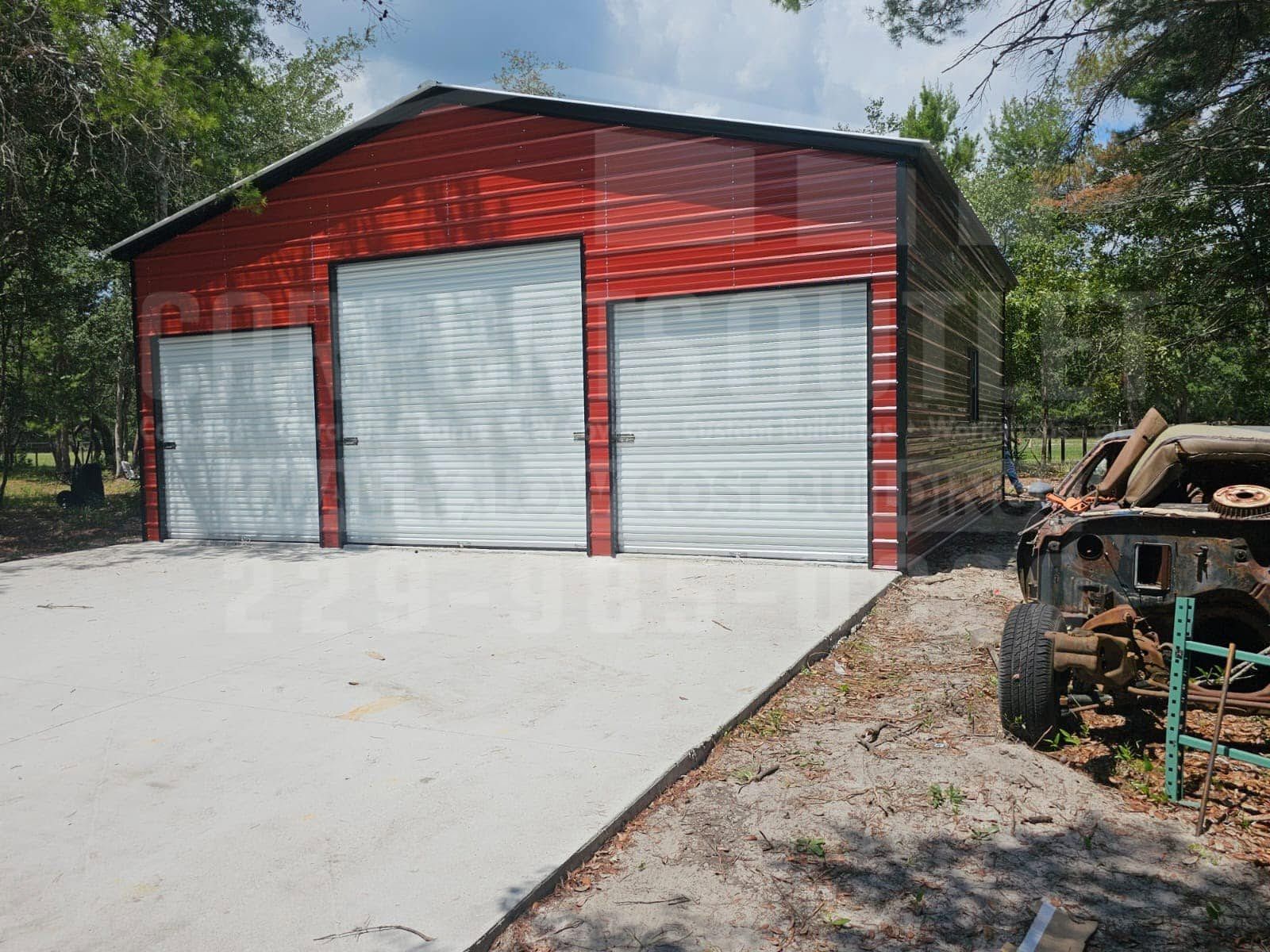 Red metal garage with three white roll-up doors beside a concrete driveway and trees