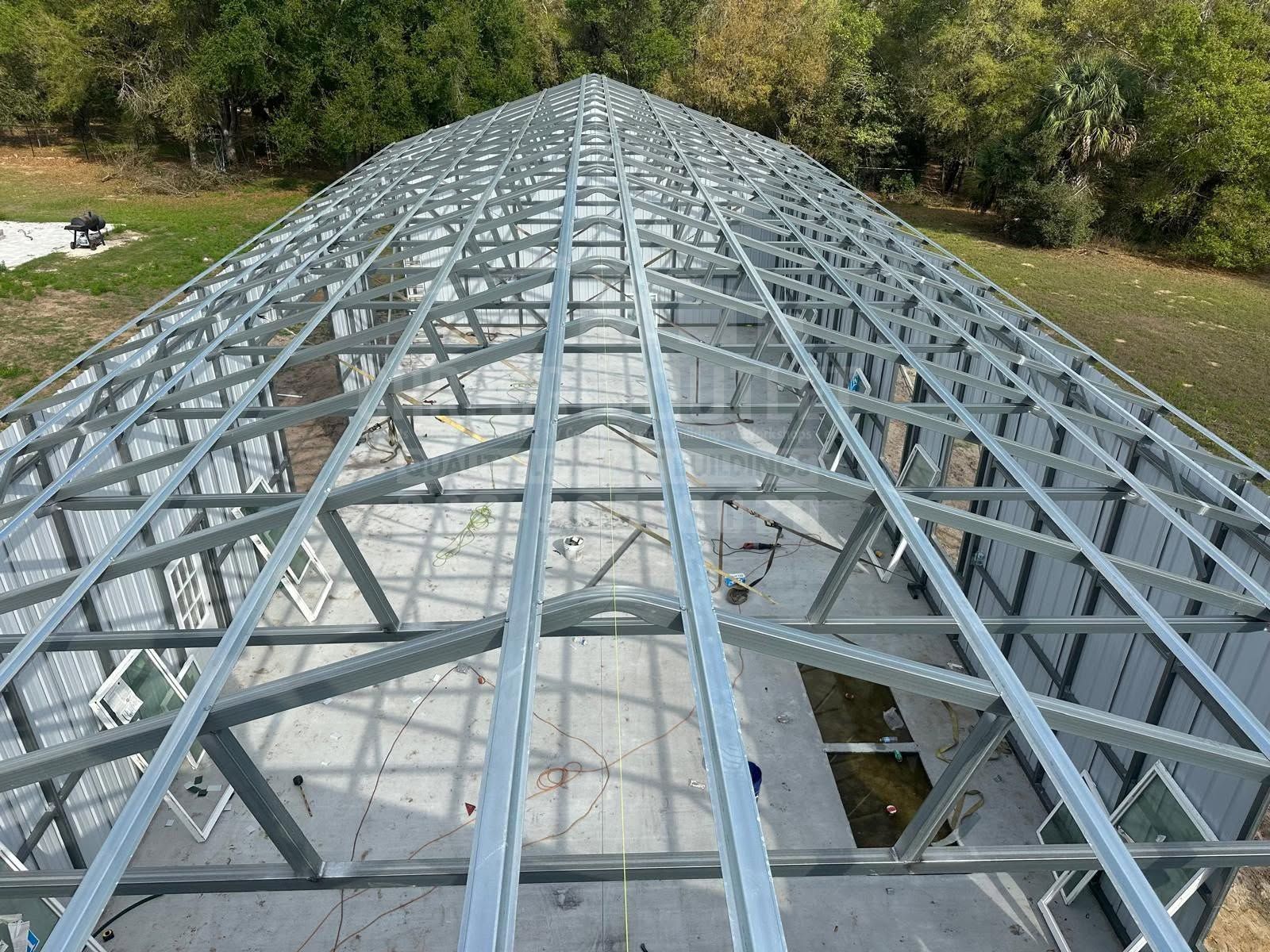 Steel roof truss framework over a building under construction, viewed from the peak looking downward.