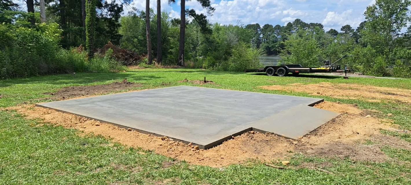 Concrete slab in a grassy clearing near trees, with a trailer in the background.