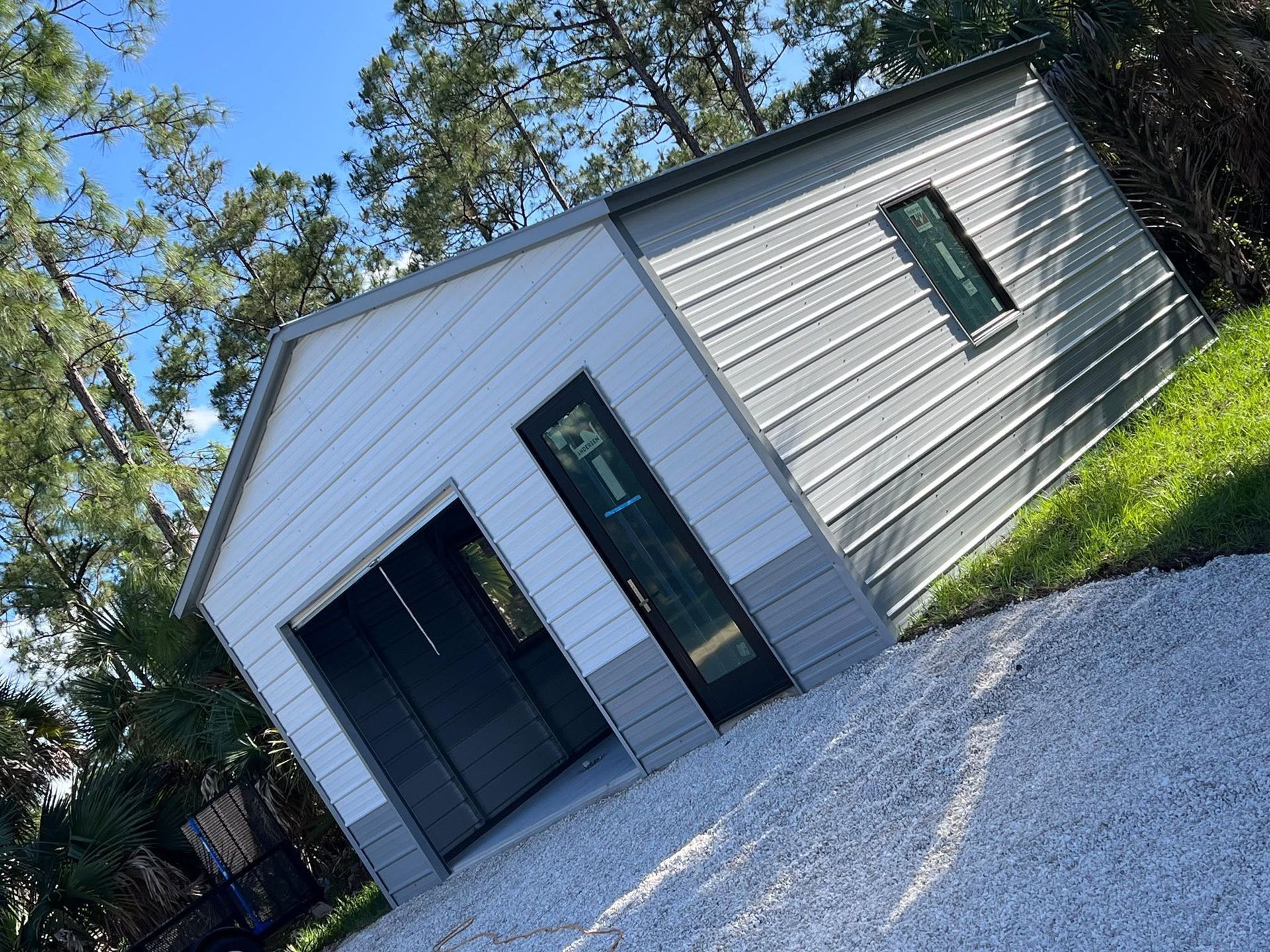Small gray house with a dark front door, narrow windows, and gravel yard, viewed at a slight angle