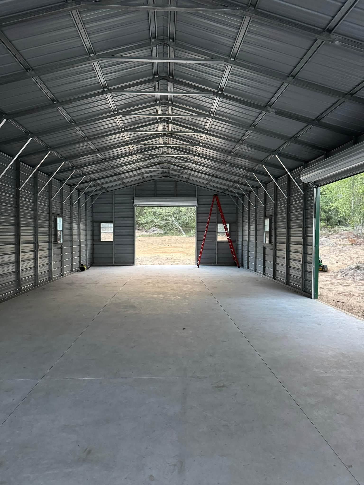 Empty metal storage shed with concrete floor and open doorway, showing a red ladder inside.