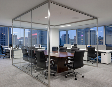 Glass-walled conference room with a large wooden table and black office chairs in a modern office building.