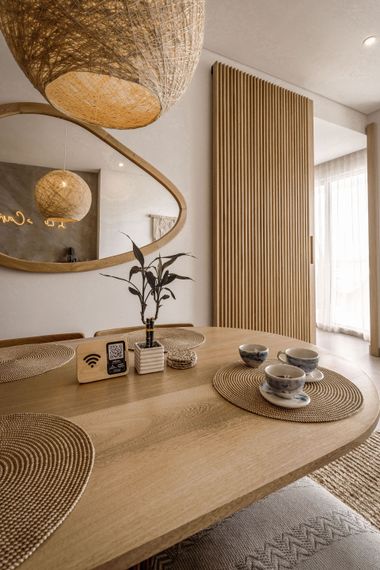 Warm beige dining room with woven pendant lights, oval mirror, textured table, and sheer curtains