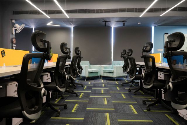 Modern office with rows of black chairs, yellow desks, and a gray couch under LED ceiling lights