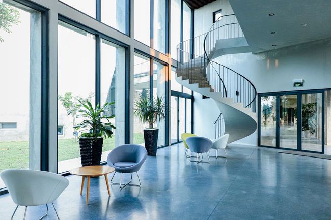 Bright modern lobby with large windows, white chairs, potted plants, and a spiral staircase