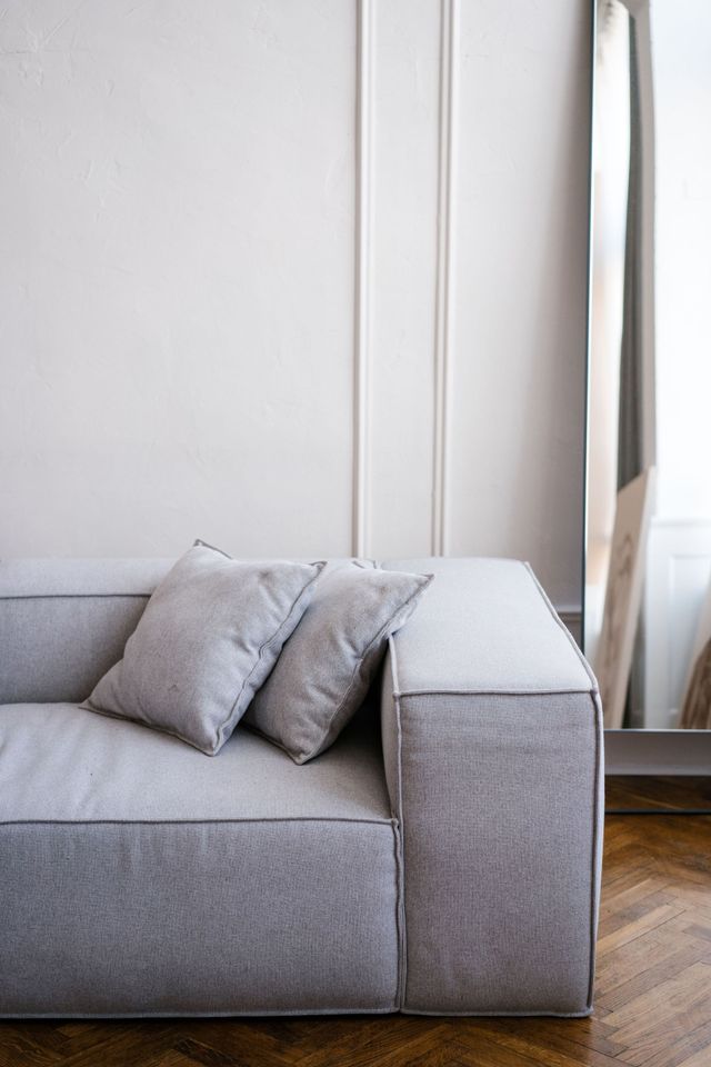 Gray sofa with two pillows beside a tall window and curtain in a bright room