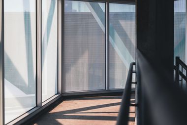 Empty sunlit hallway with glass walls, railing, and diagonal shadows on the floor