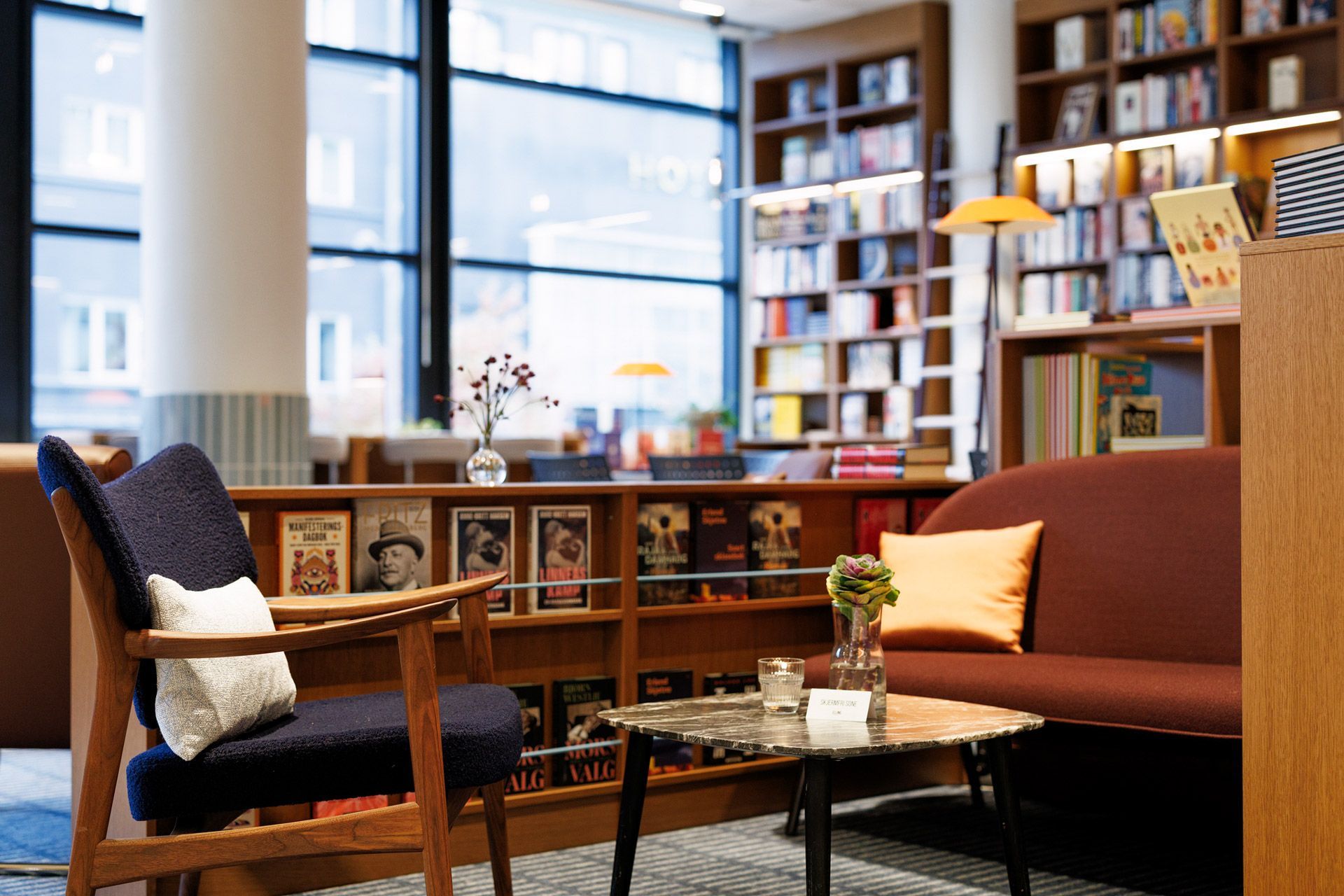 Koselig sittegruppe i biblioteket med lenestoler, salongbord, bokhyller og store vinduer