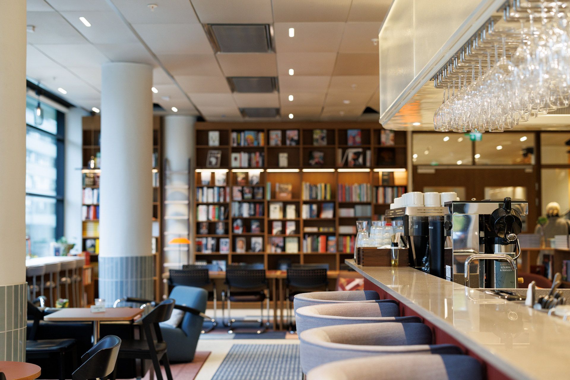 Moderne kaféinteriør med bokhyller, barstoler og varm pendelbelysning
