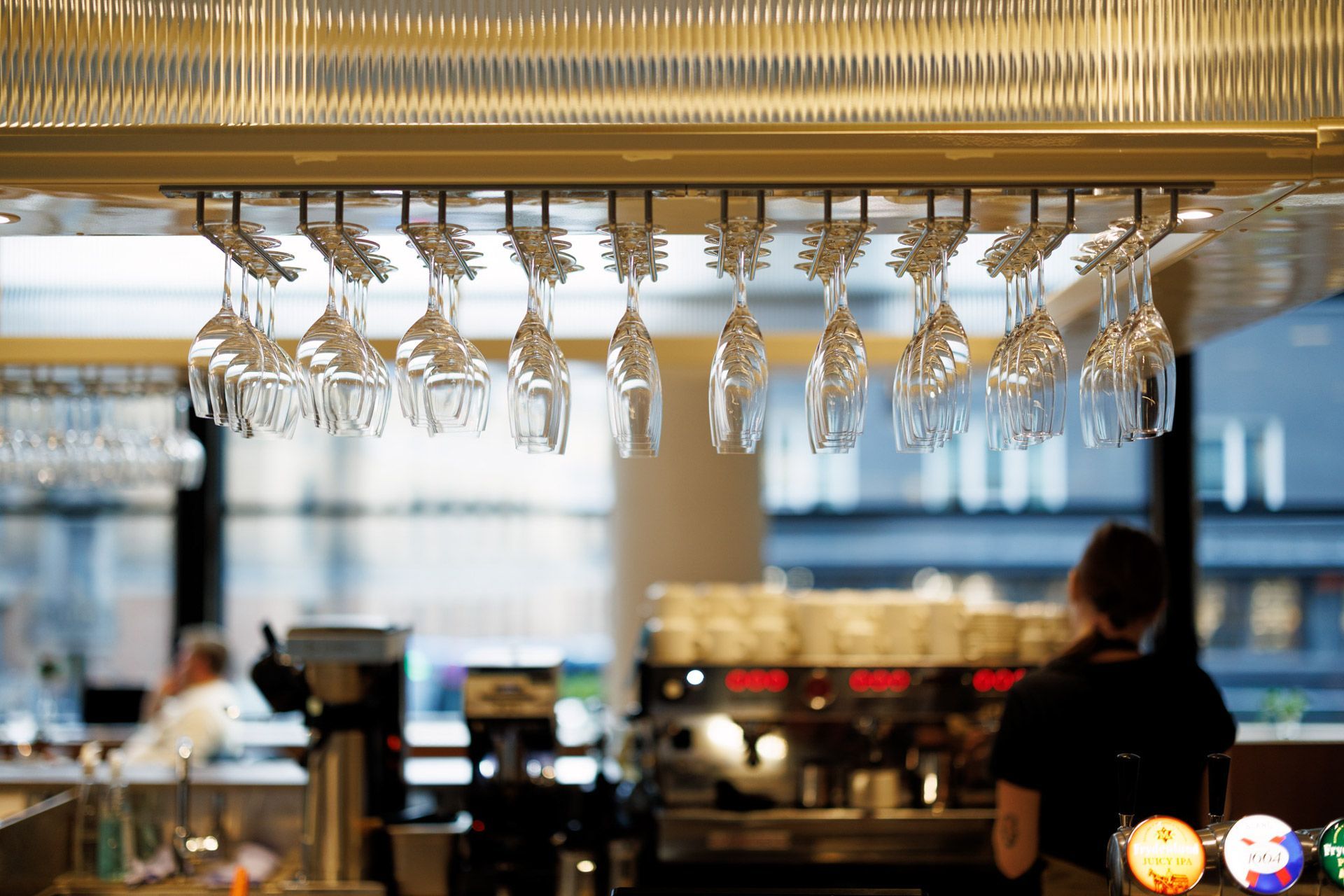 Rader med hengende vinglass over en bar med en bartender i en mykt opplyst restaurant