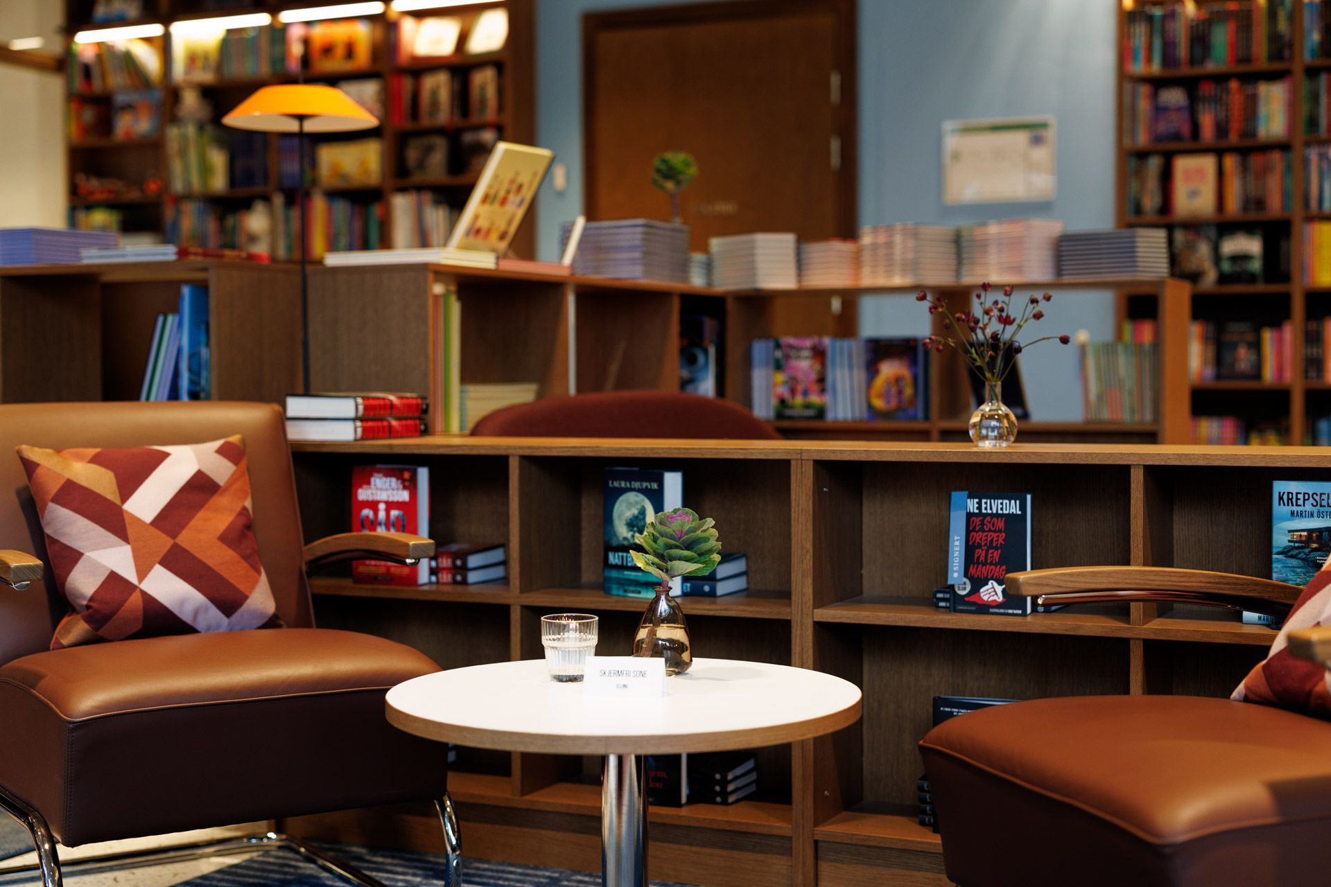 Koselig bibliotekstue med bokhyller, brune stoler og et lite hvitt bord med kopper og blomster