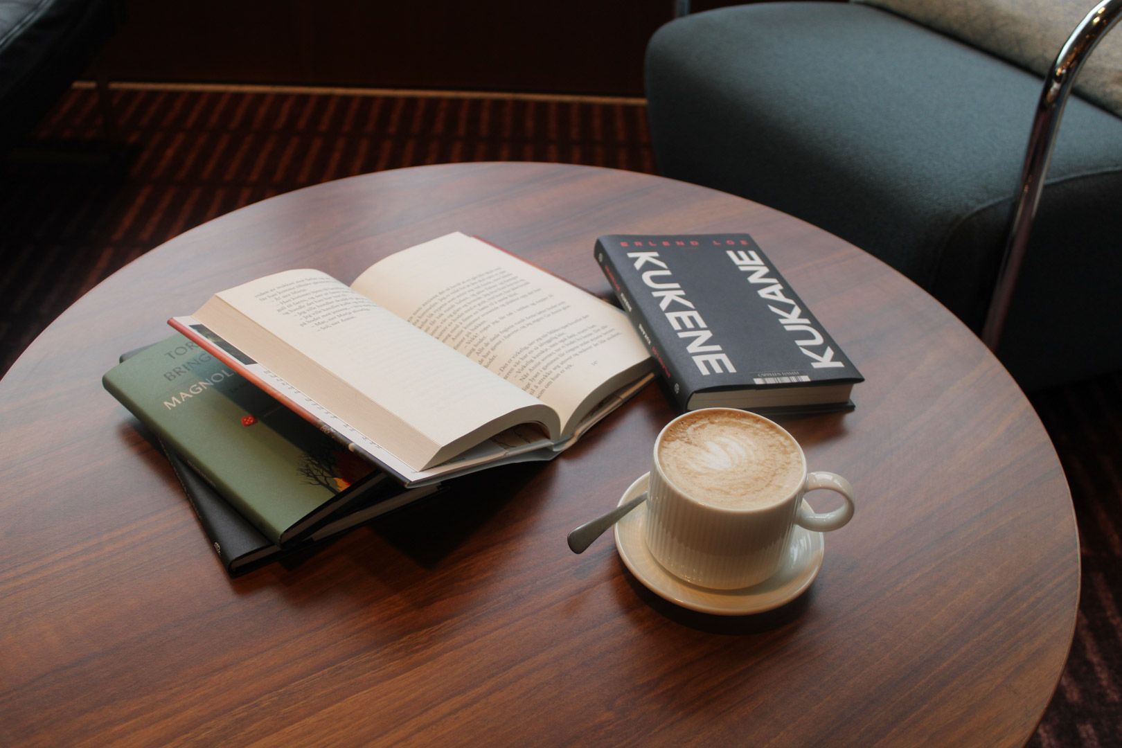 Åpen bok og kaffekopp på et trebord ved siden av en vindussete