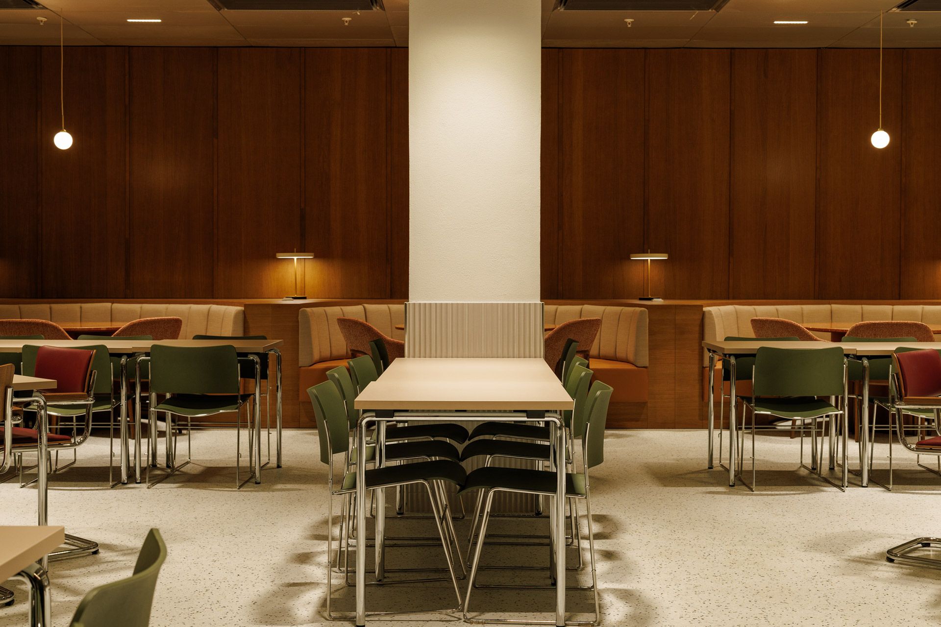 Moderne kafé-spisestue med bord, stoler, varme trevegger og en sentral søyle.