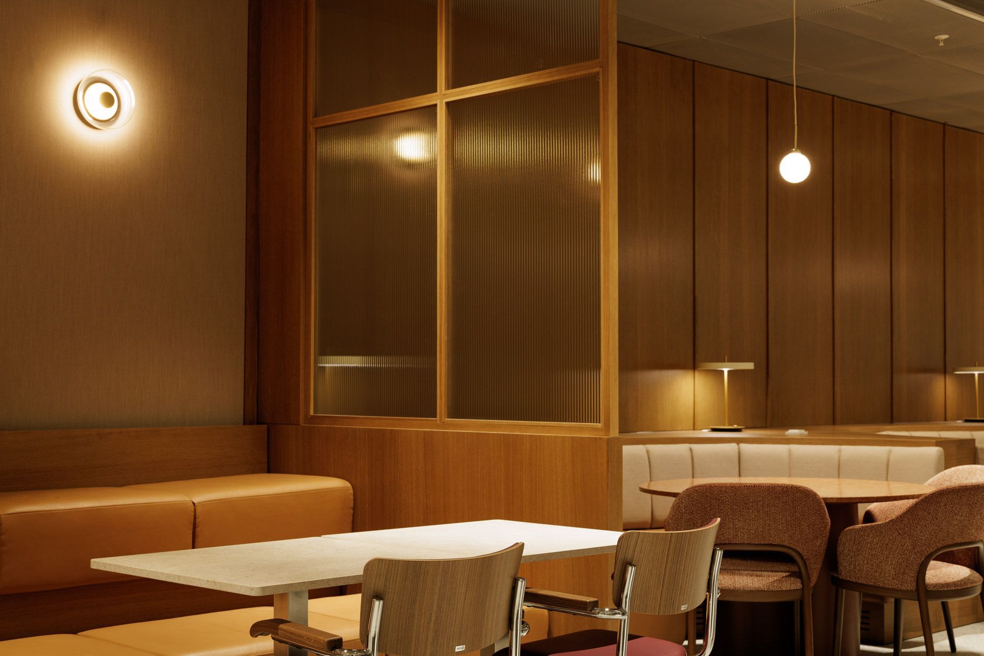 Tomt, moderne restaurantinteriør med varme trepaneler, runde vegglamper og bord og stoler