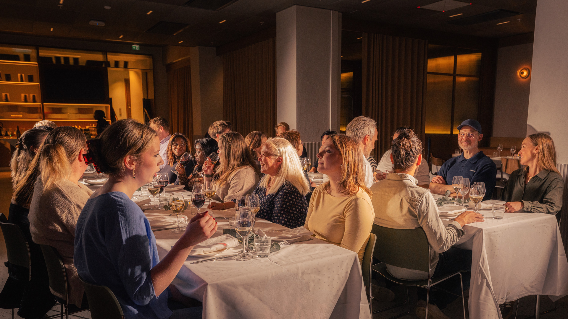 Varmt, svakt opplyst bar- og loungeinteriør med runde bord, skinnseter og hengende globuslys