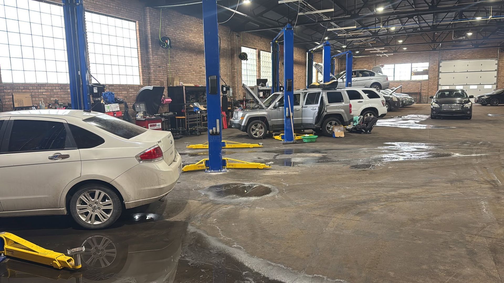 Car repair shop with several cars on lifts and wet concrete floor inside a garage | The Garage MKG