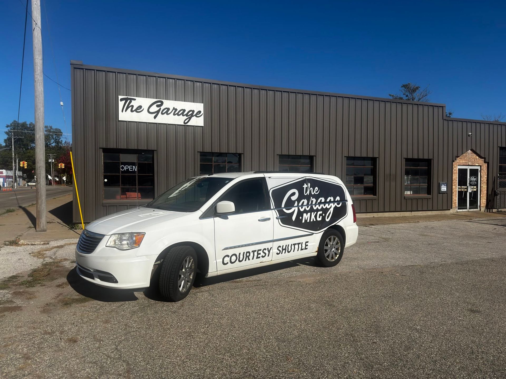 White delivery van parked outside The Garage building on a gravel lot, with cloudy sky overhead. | The Garage MKG