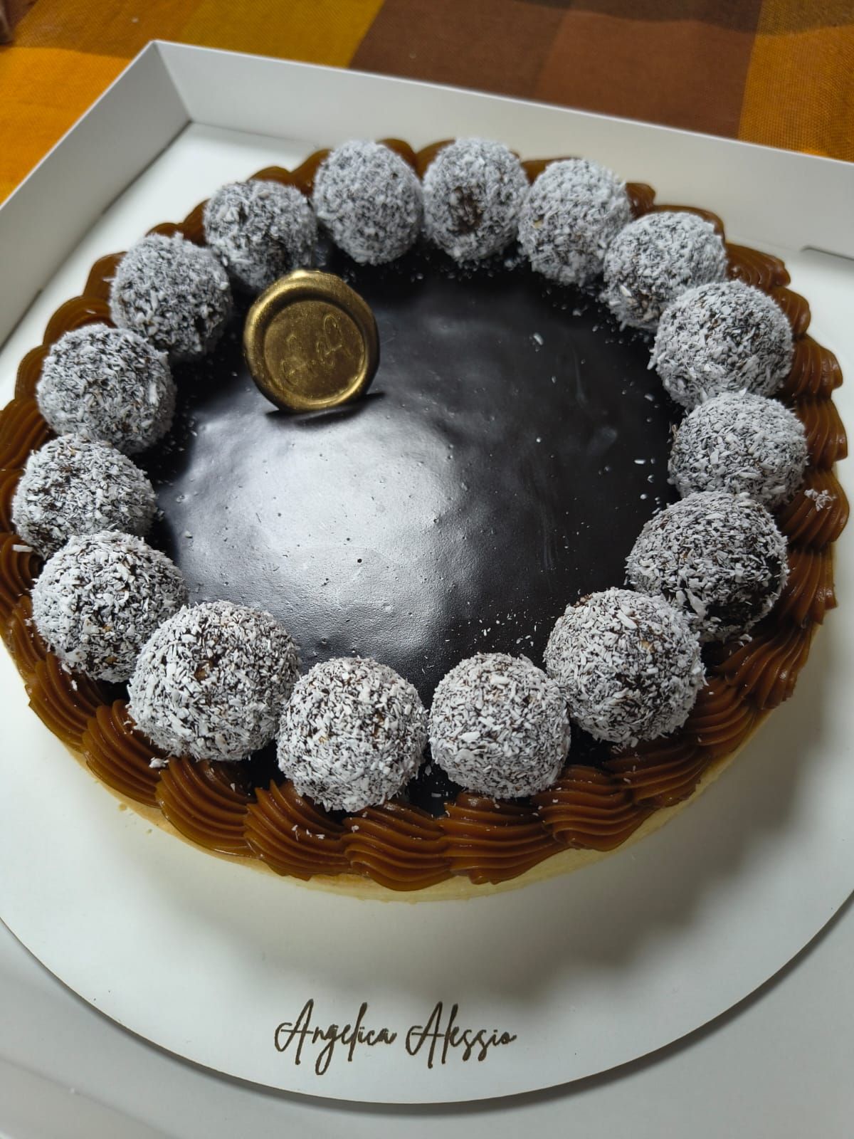 Pastel de chocolate cubierto con trufas de coco, decorado con una moneda de oro sobre un plato blanco.