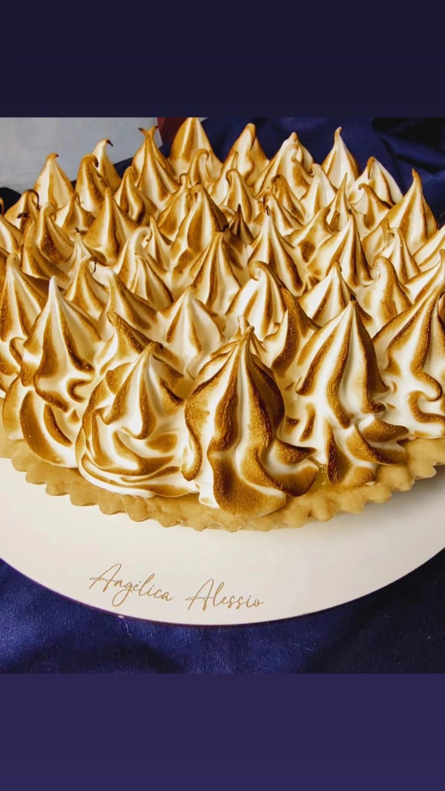 Pastel blanco cubierto con espirales doradas de merengue sobre un mantel morado oscuro.