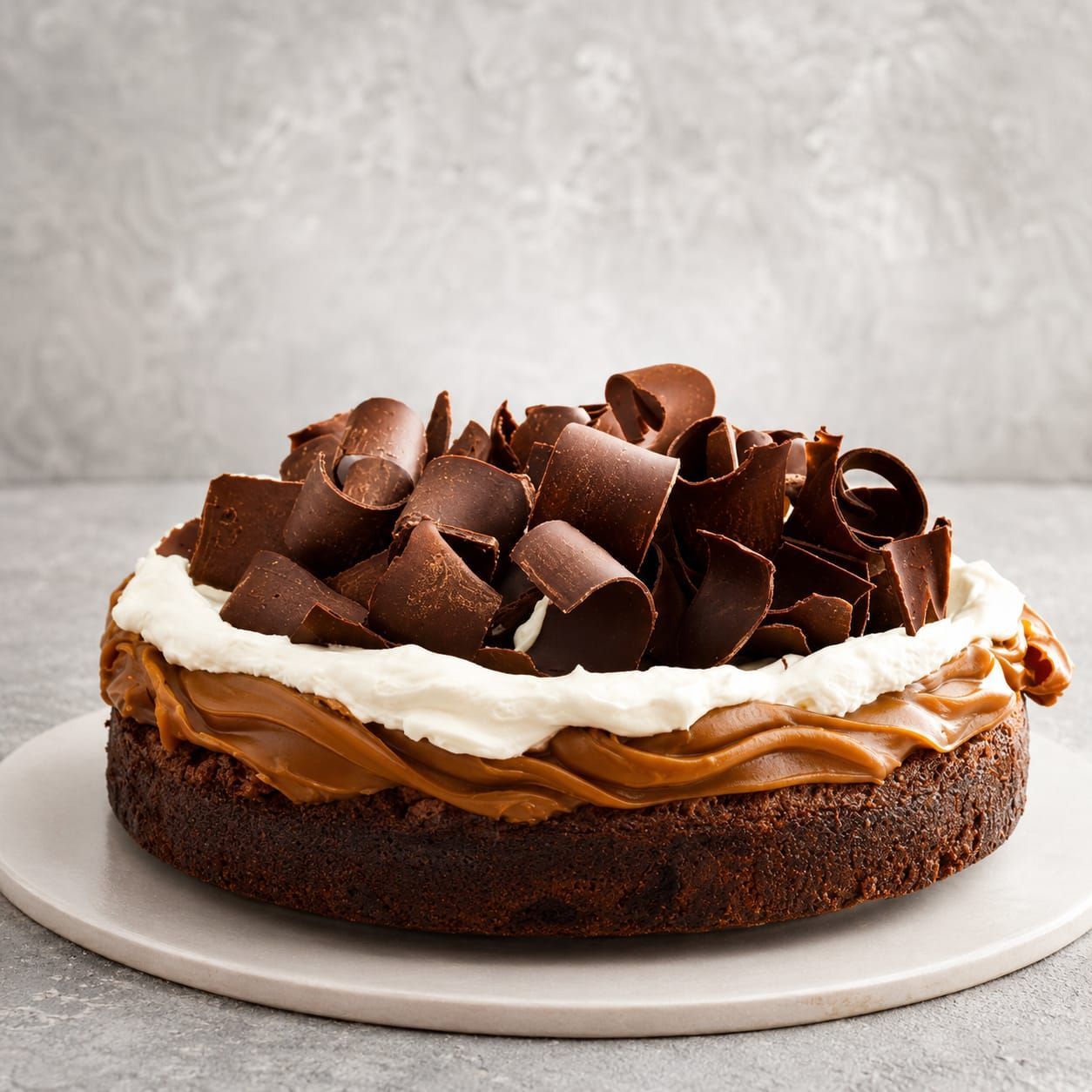Pastel de chocolate con glaseado blanco y rizos de chocolate en un plato blanco.
