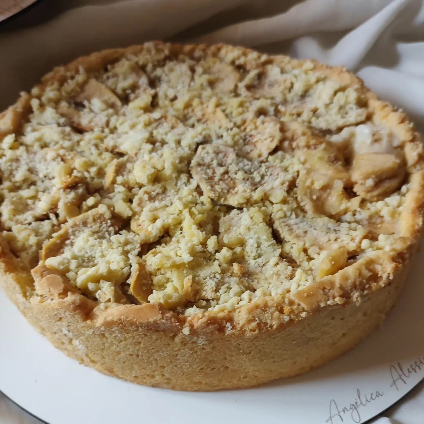 Primer plano de una tarta o pastel redondo cubierto con una capa de migas sobre un plato blanco.