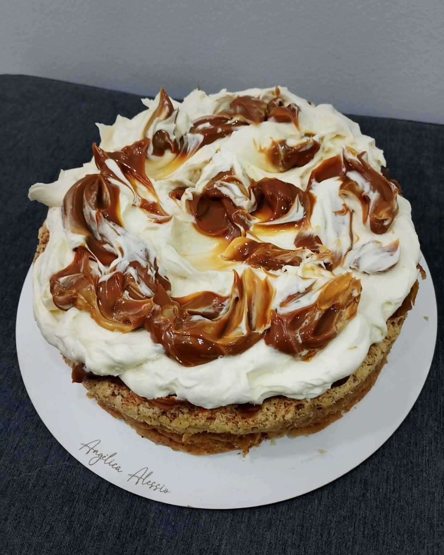 Pastel redondo cubierto con crema blanca y espirales de caramelo sobre un plato blanco.