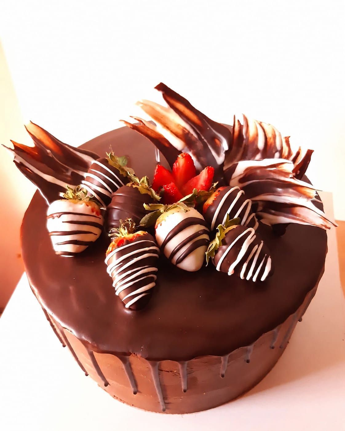 Tarta de chocolate cubierta con fresas bañadas en chocolate y plumas de chocolate negro.
