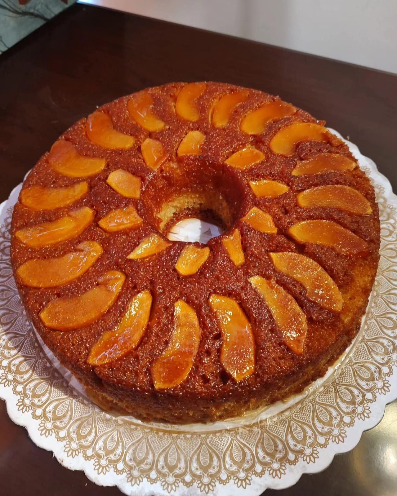 Pastel redondo glaseado con melocotón, con rodajas de melocotón dispuestas en círculo sobre un plato decorativo.