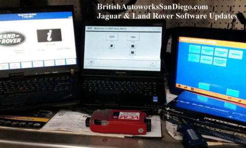 Three laptops on a desk displaying Jaguar and Land Rover software update screens, with a red device in front